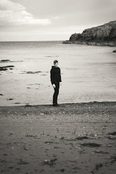 Artistic black and white portrait of a person standing alone on a desolate beach.