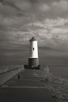 A striking black and white image of a solitary lighthouse against an overcast sky by the sea.