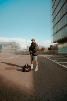 Casual man in urban parking area with bag, wearing casual attire and sunglasses.