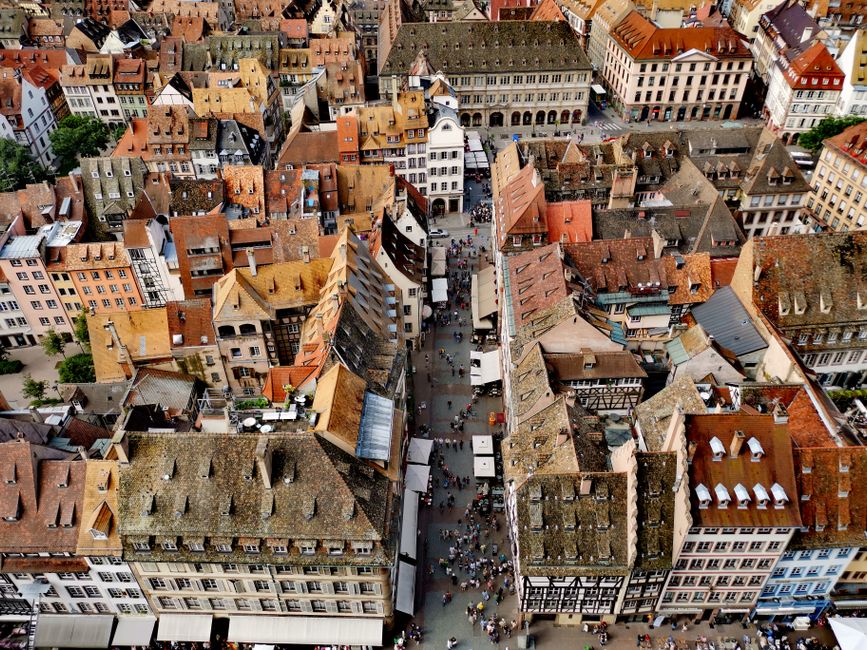 Drone view of historic rooftops and streets in Strasbourg, France with vibrant crowds.