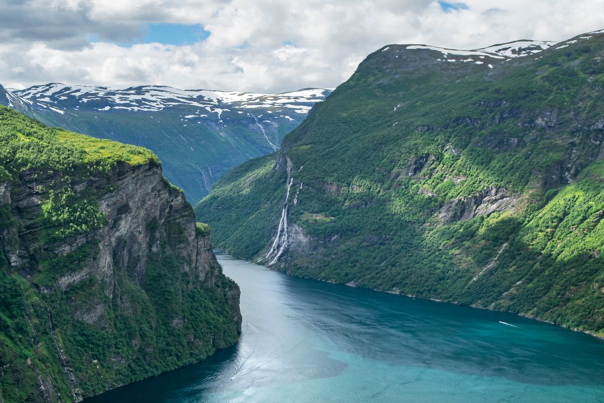 Breathtaking view of Geirangerfjord cliffs and waterfall under a bright sky in Norway.