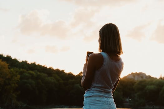 A woman with short hair captures a breathtaking sunset using her phone.