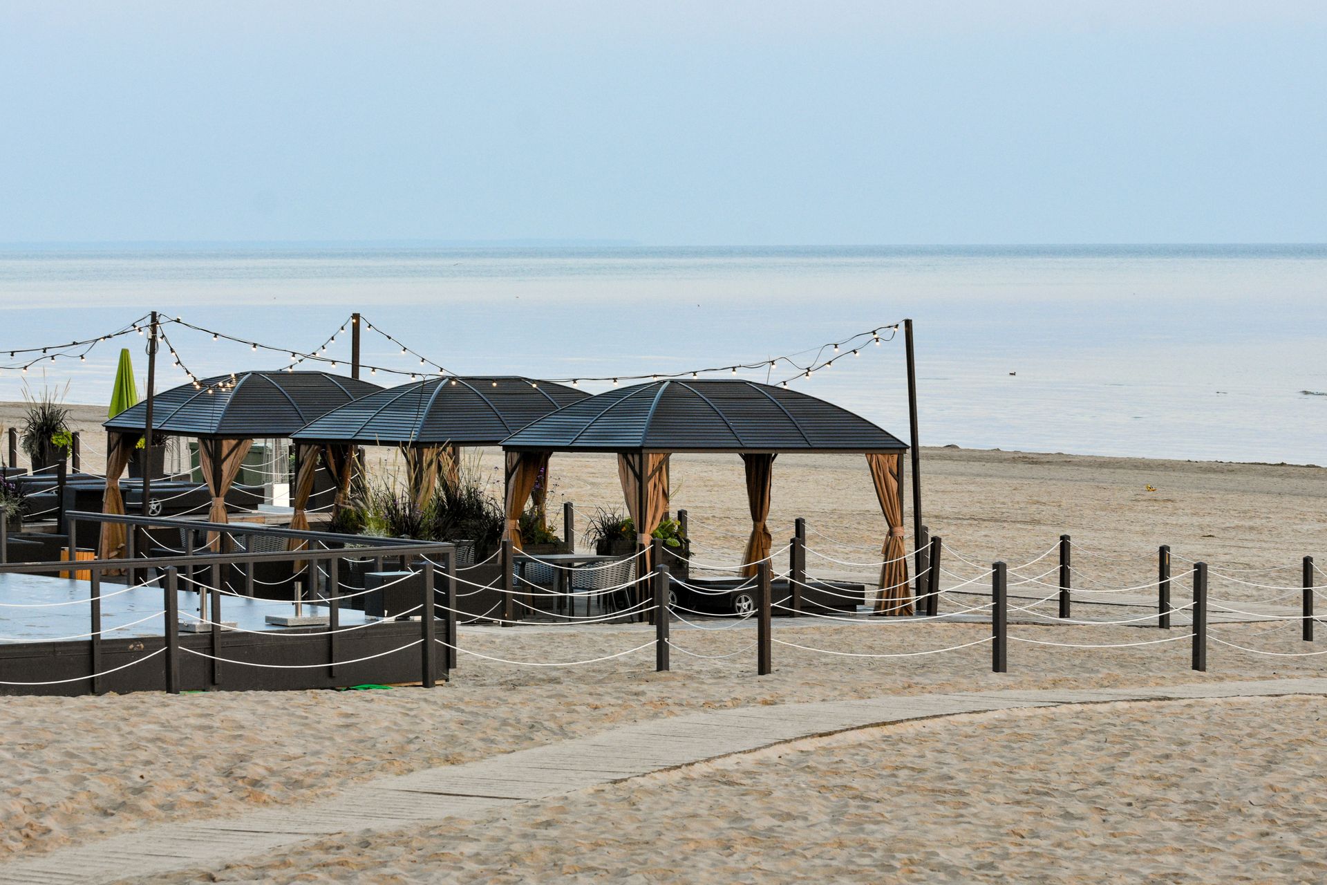 A serene beach scene featuring gazebos with string lights and a view of the calm sea.