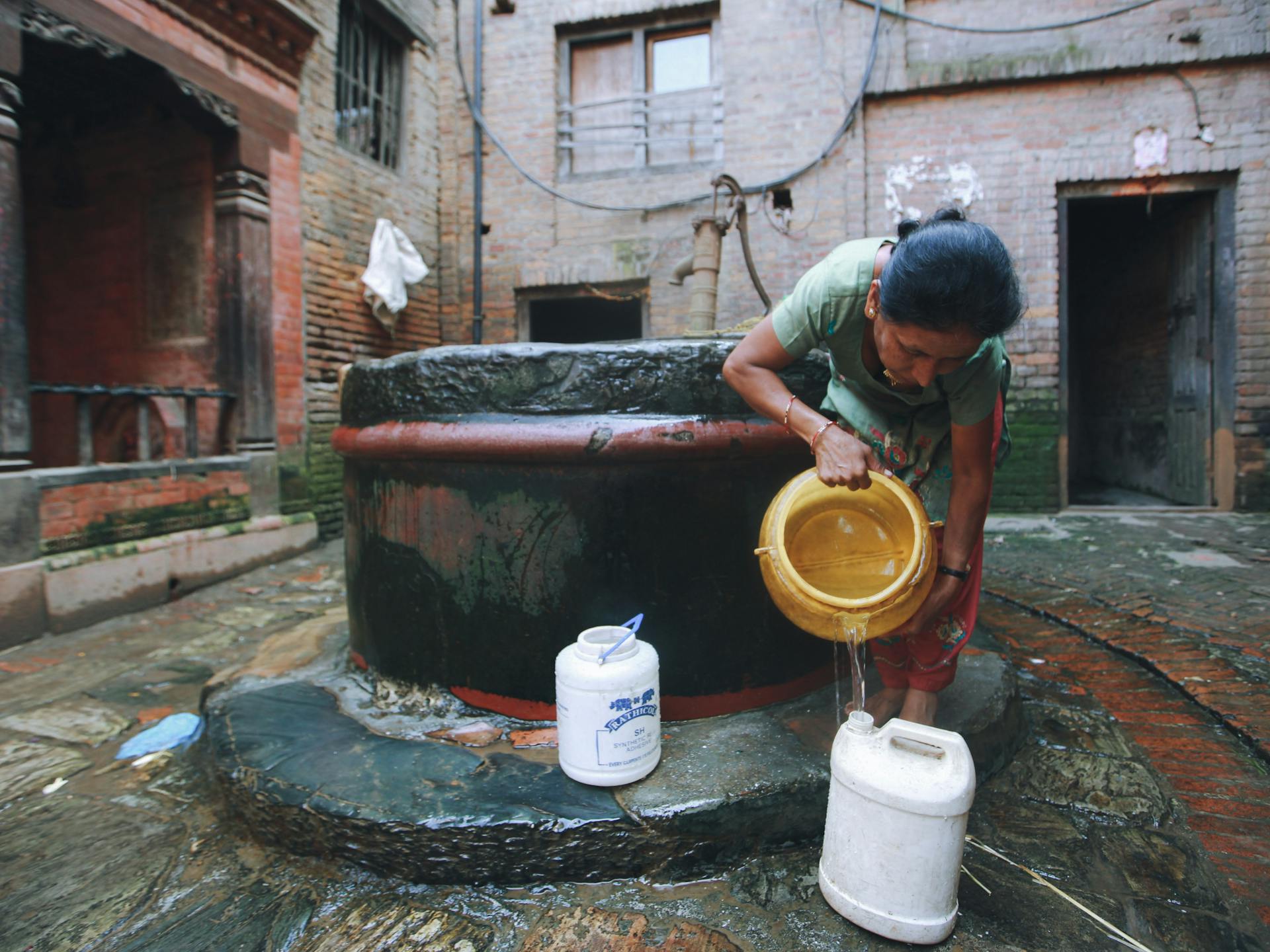 A woman filling containers with water from a rustic well in a courtyard.