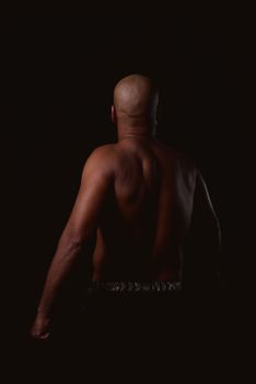 Bald man with muscular back in a dark studio setting, showcasing strength and physique.