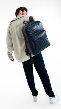 A man in a modern fashion outfit carrying a leather backpack.