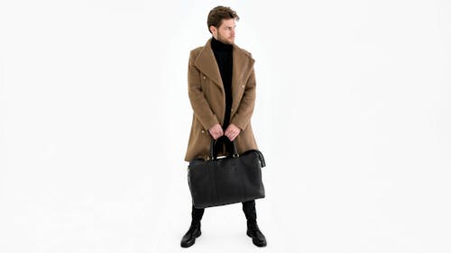 A Man in a Brown Coat Holding a Black Duffel Bag