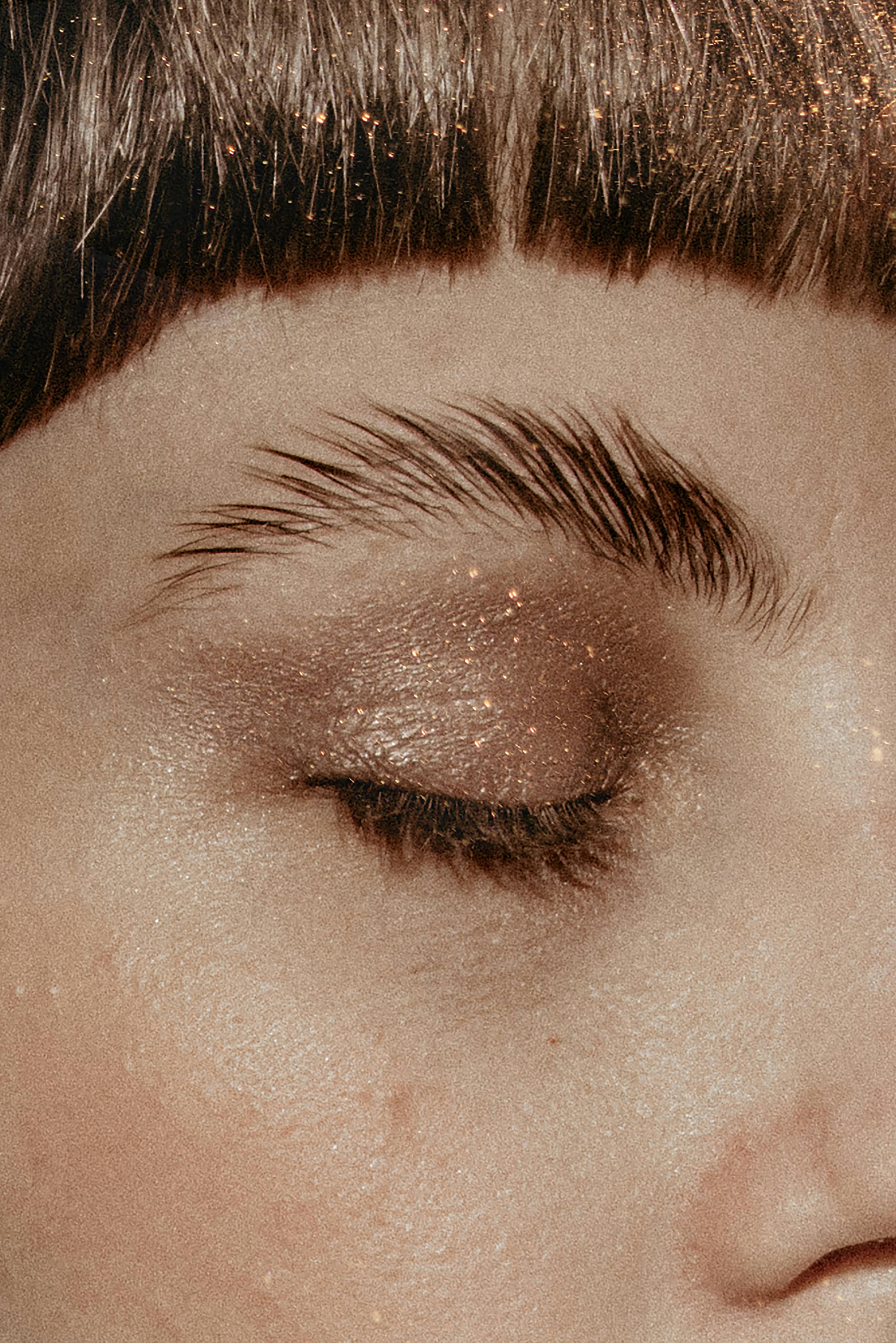 A detailed close-up of a woman's eye with glittery eyeshadow in a monochrome palette.