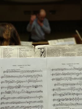 Detailed shot of sheet music during a symphony rehearsal, conductor in the background.