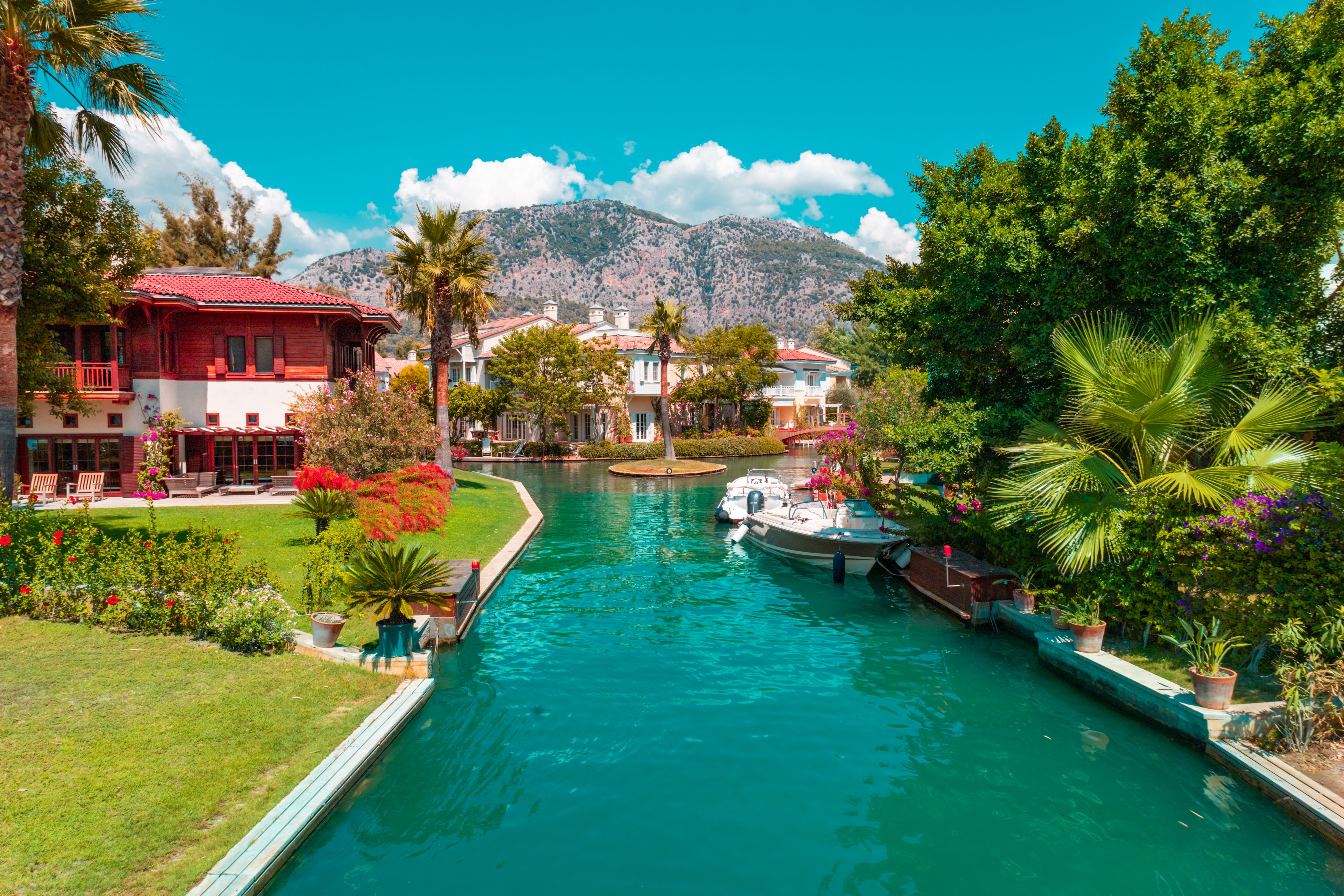 Explore the picturesque Göcek canal with lush greenery, villas, and boats, set against a mountain backdrop.