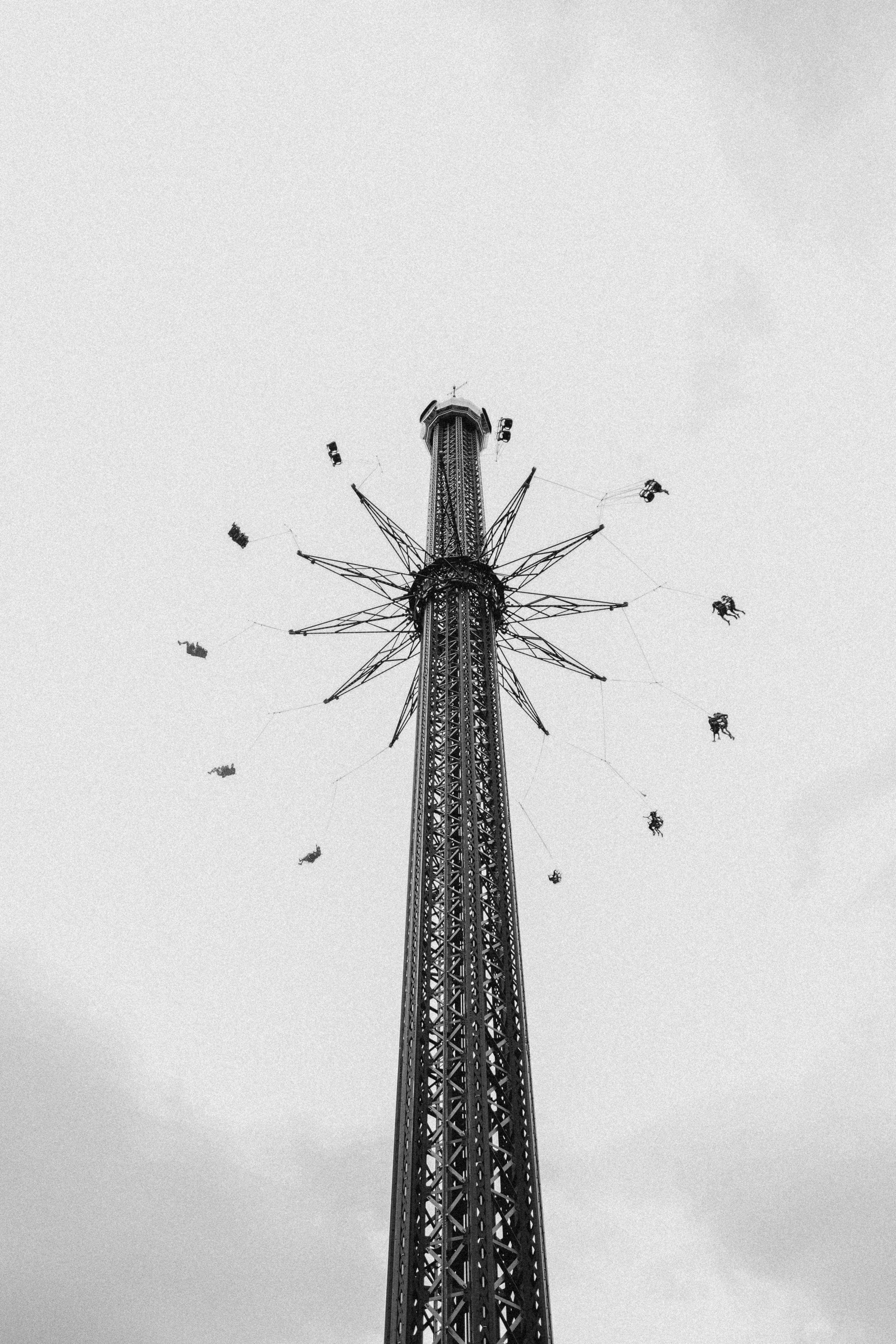 Black and white photo of a tall chain swing ride against a cloudy sky, emphasizing motion and height.