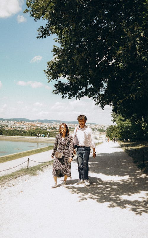 Woman and Man Walking on Footpath under Trees