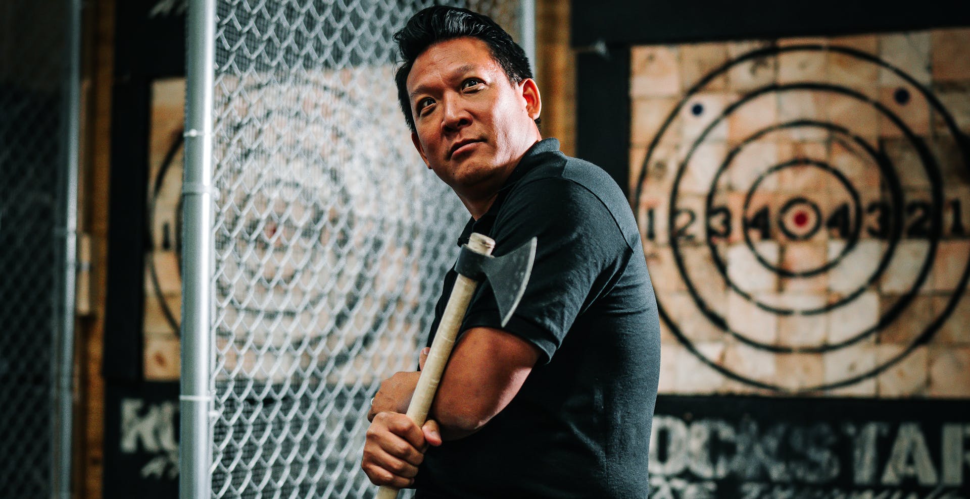 Man posing with an axe in an indoor axe throwing facility, ready for sport.