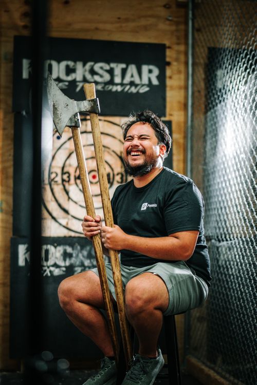 Free Smiling man holding axes in an indoor throwing venue, showcasing joy and leisure. Stock Photo