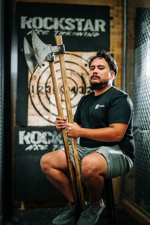 Free Man sitting with axes at an indoor axe throwing range, ready for a session. Stock Photo