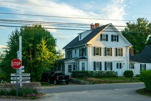 Quaint colonial house at suburban street with cars and road signs under clear sky.