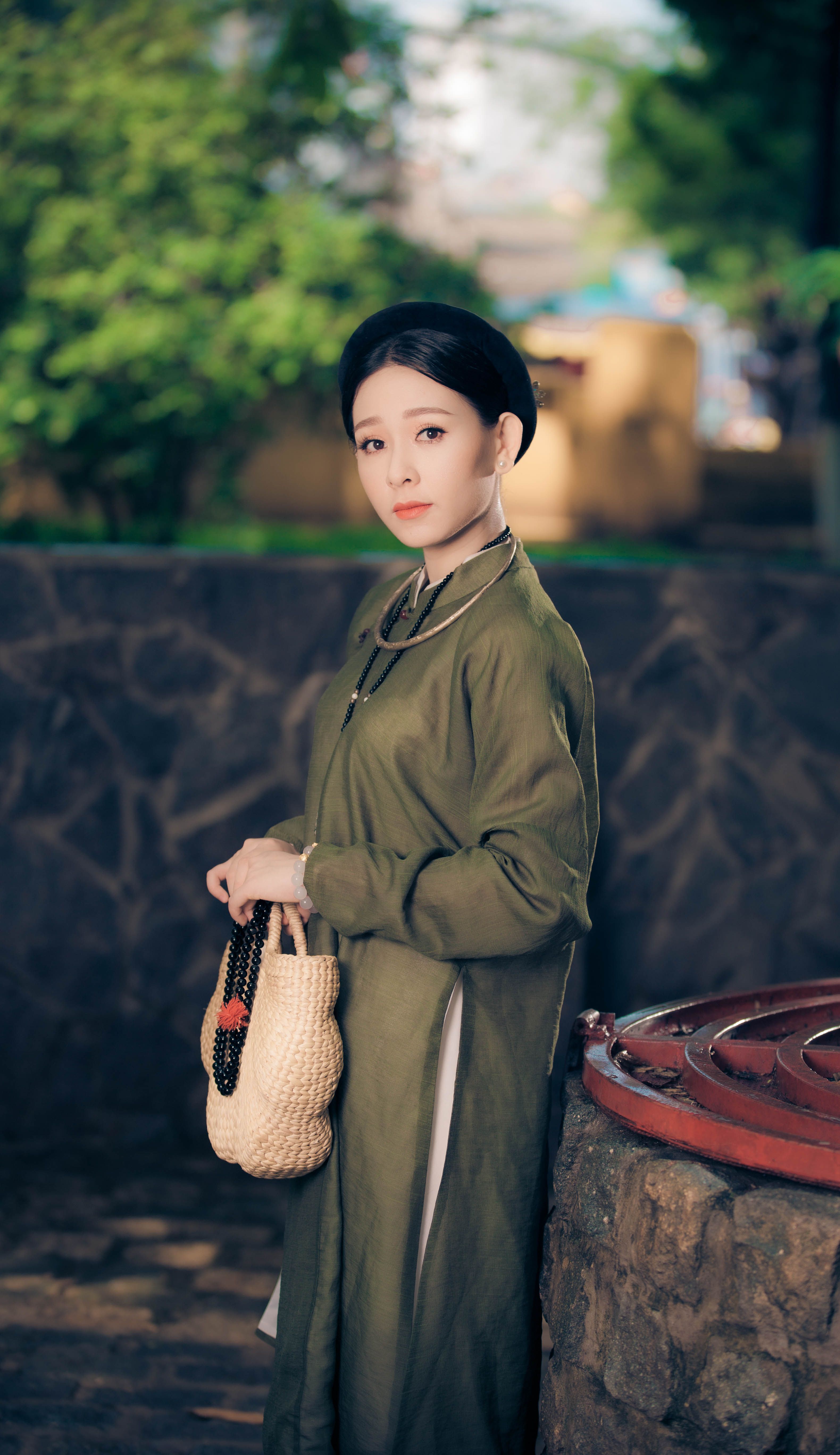 A serene scene of a woman in a green ao dai holding a basket, set against an outdoor background.