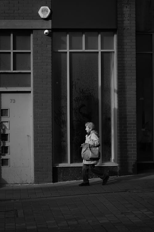 Grayscale Photo of a Woman Walking on the Sidewalk
