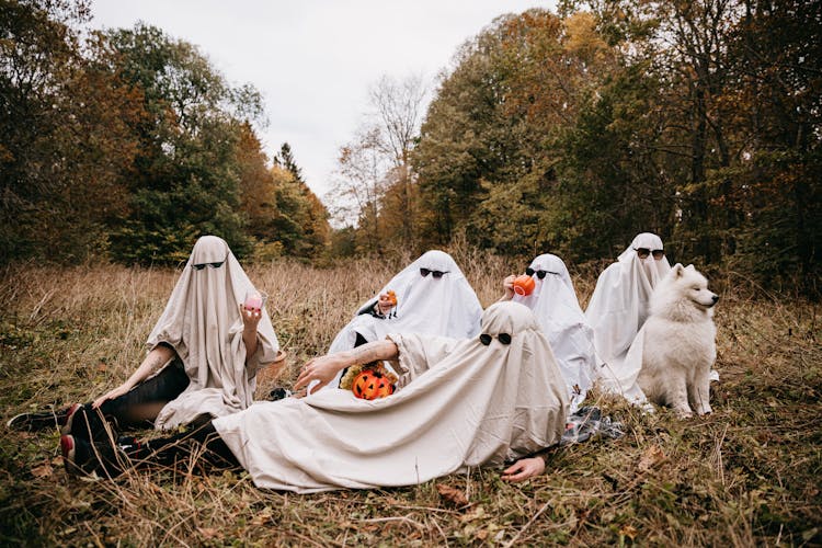 People In Halloween Ghost Costumes Sitting On Grass