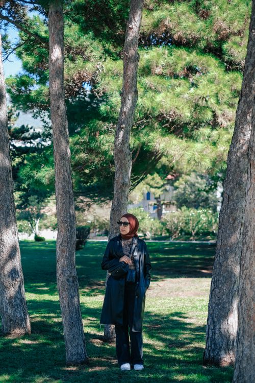 Free A woman in a hijab stands outdoors among tall trees, enjoying a sunny day in a park. Stock Photo