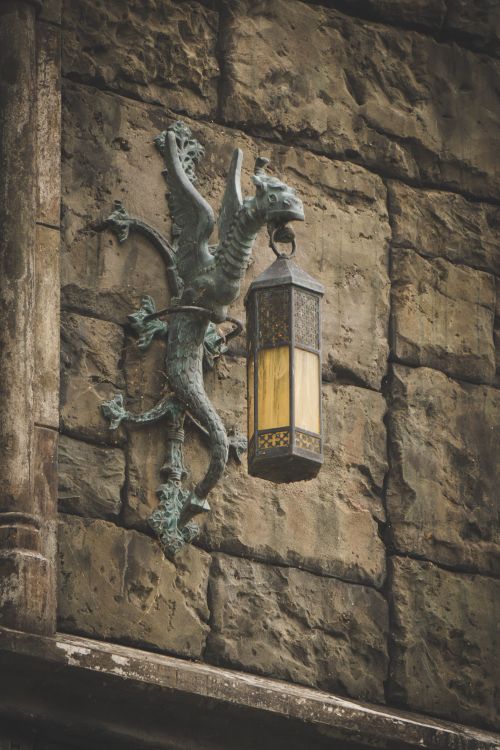 Free A gothic-style dragon sculpture holding a lantern mounted on a stone wall. Stock Photo
