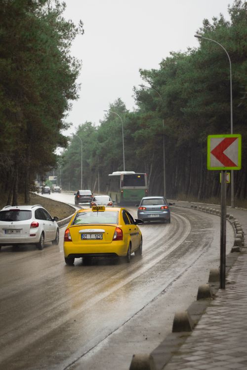 Free Traffic on a wet road in Adana, Türkiye after rain with a visible yellow taxi and green trees. Stock Photo