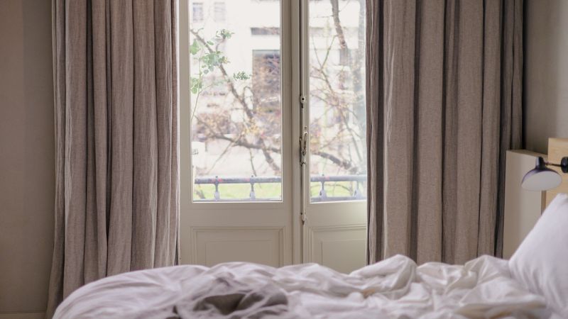 White-backed blackout curtains drawn closed over a large bedroom window to block bright summer sunlight