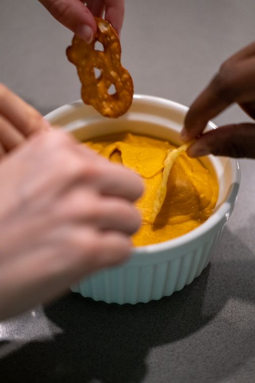 Free Hands dipping pretzels and chips into a bowl of creamy dip, perfect for appetizers. Stock Photo