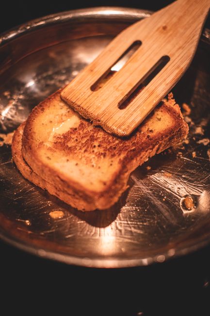 A stack of toasted crumpets with golden brown tops, visible holes filled with melted butter, and a drizzle of honey running down the side.