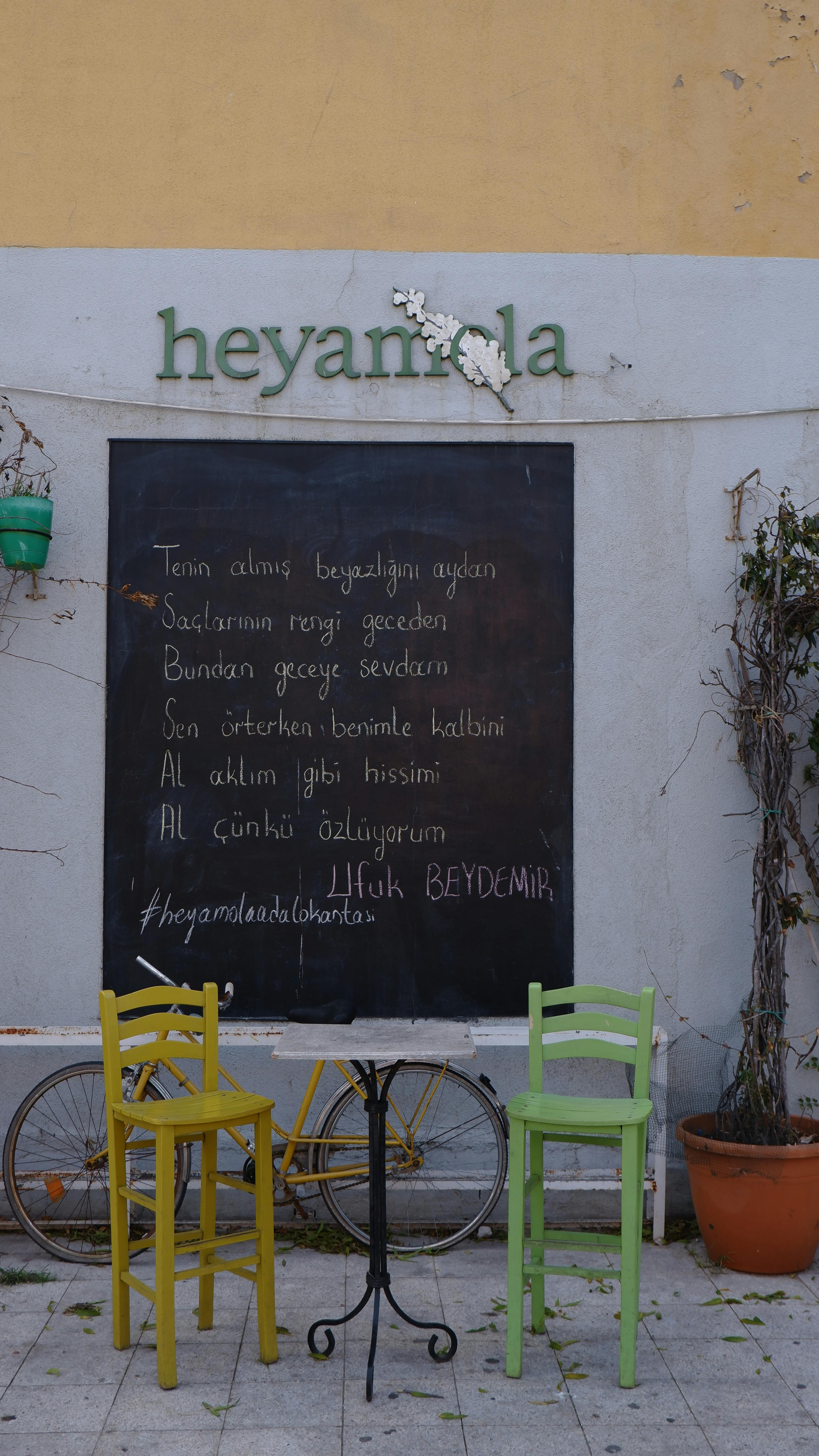Outdoor cafe scene with colorful chairs and a bicycle against a chalkboard wall.