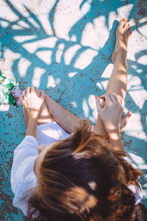 Free A young woman sitting barefoot on a sunny surface with vibrant shadows around her. Stock Photo