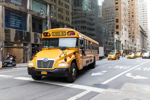 Free A yellow school bus navigates a busy New York City street amidst tall buildings and taxis. Stock Photo