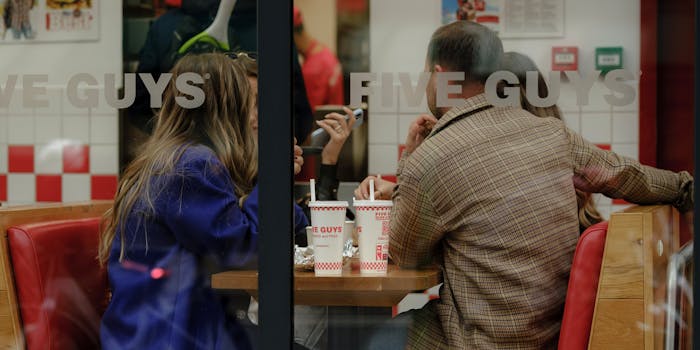 A group of friends share a meal and conversation at Five Guys, visible through the window.