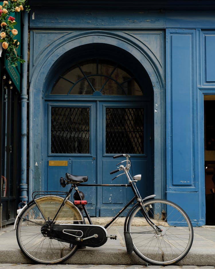 Black Bicycle Parked In Front Of Blue Building