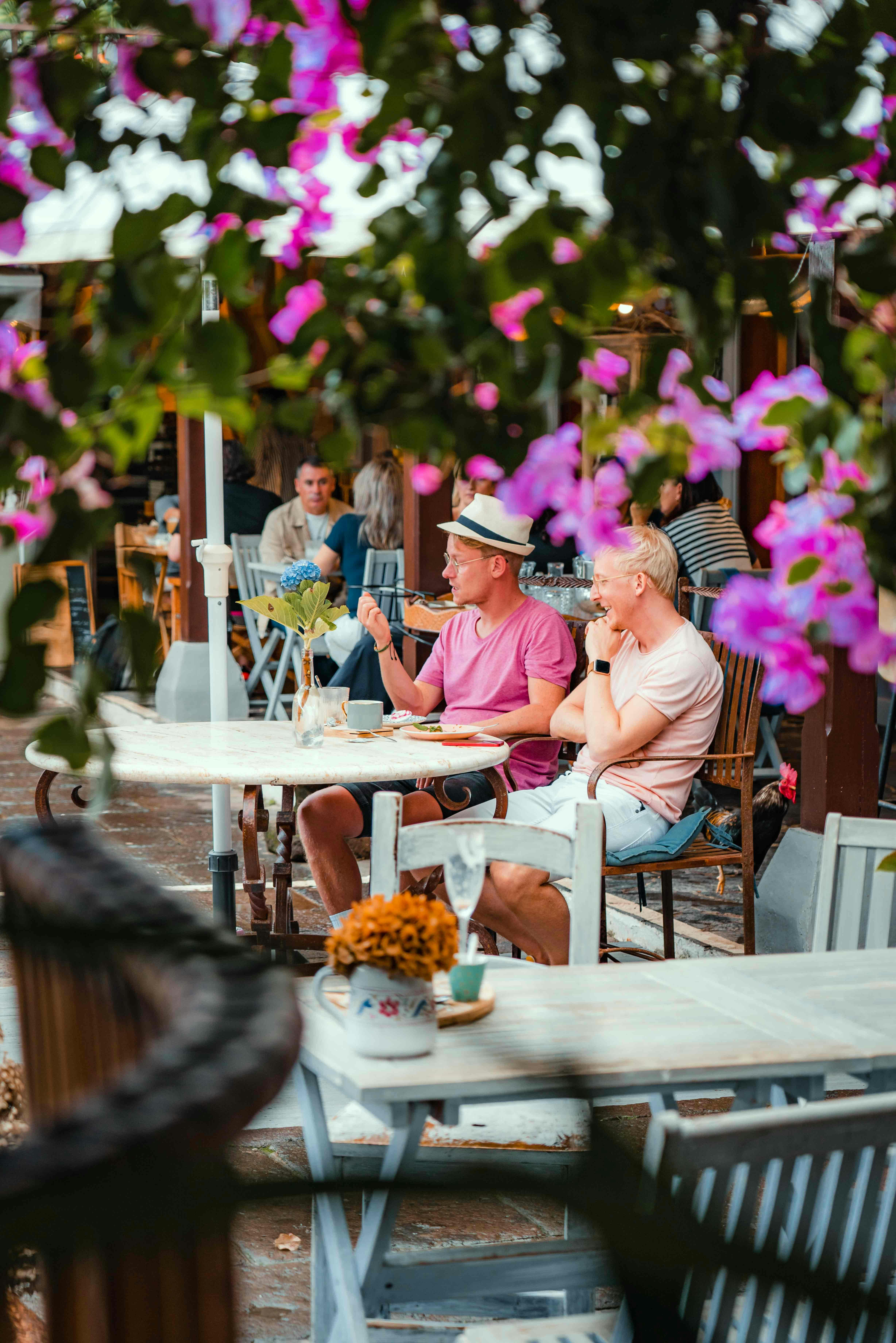 Two men enjoy a relaxing time at an outdoor café surrounded by vibrant flowers.