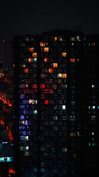 A striking view of a city building at night with vibrant illuminated windows showcasing various colors.