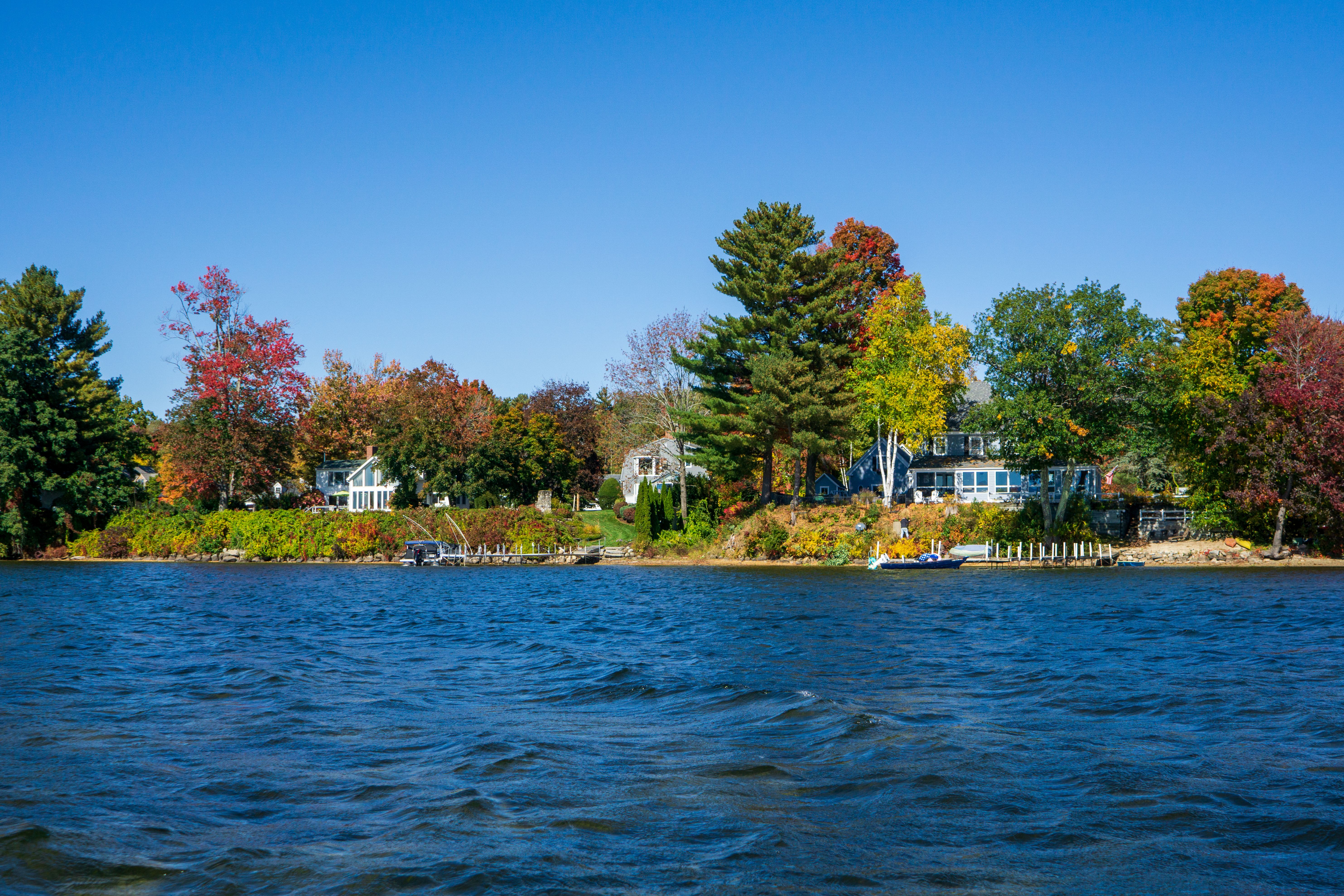Charming lakeside houses surrounded by vibrant autumn foliage under a clear blue sky.