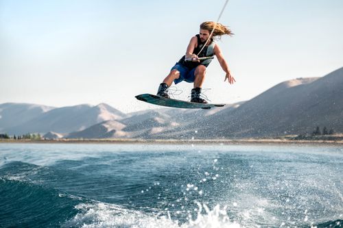 Free A man with long hair performs an aerial wakeboarding trick over a lake. Stock Photo