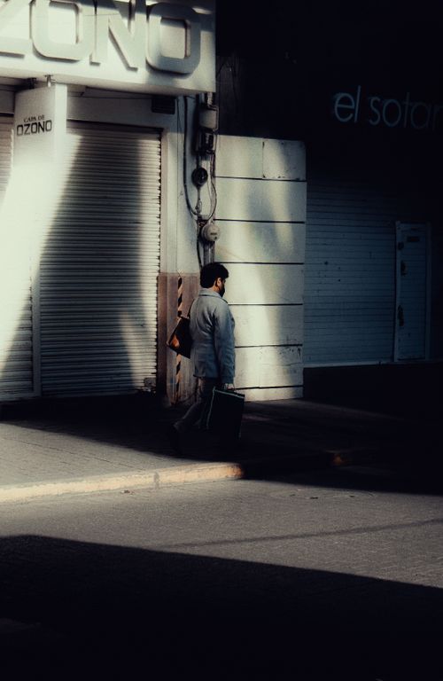 Free Man carrying briefcase on city street with dramatic shadows and urban backdrop. Stock Photo