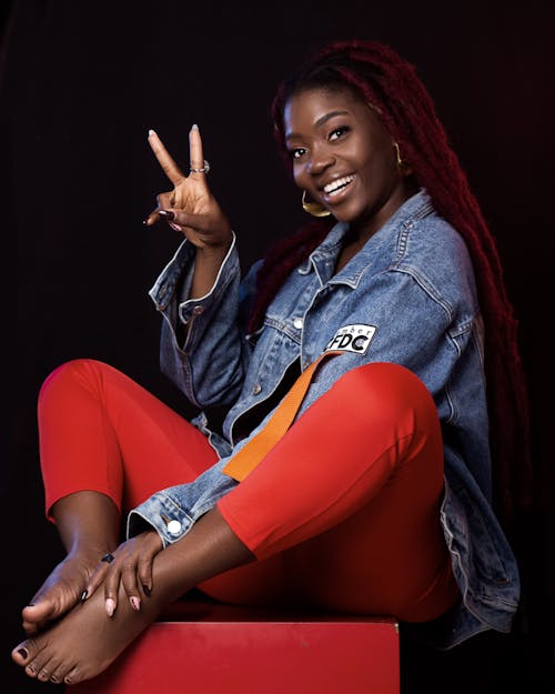 A Woman in Blue Denim Jacket and Orange Pants Sitting on a Red Chair