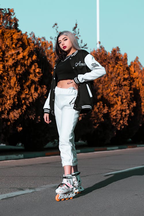 Woman in Black and White Jacket and White Pants Standing on Gray Asphalt Road