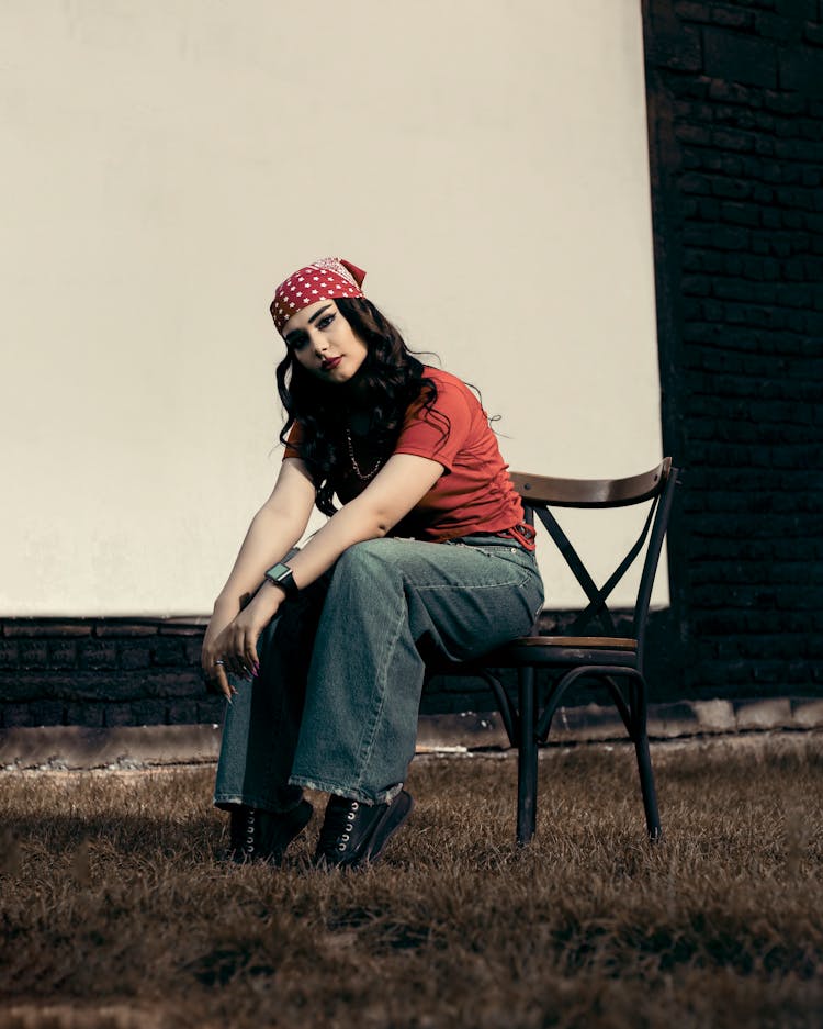 Woman In Red Shirt And Blue Denim Jeans Sitting On Brown Wooden Chair