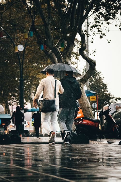Free Two people walking with umbrellas on a rainy street in İstanbul, showcasing urban life. Stock Photo