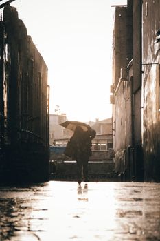 Mysterious silhouette of a person holding an umbrella in a rain-soaked alley in Istanbul during daytime.