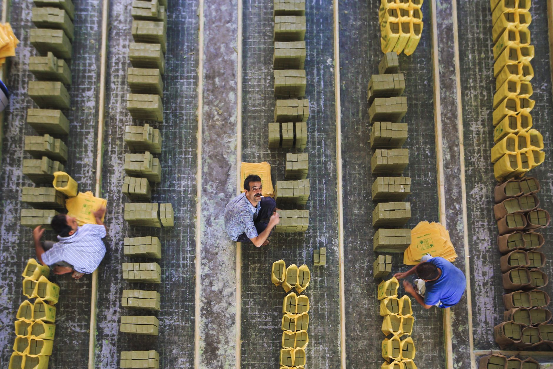 Top view of workers organizing yellow bricks in rows at an industrial factory.