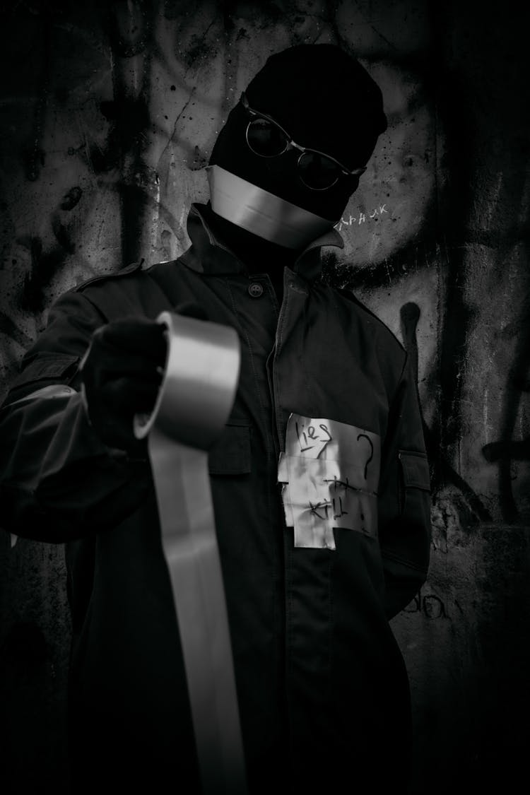 Grayscale Photo Of A Person Wearing A Mask Holding A Duct Tape