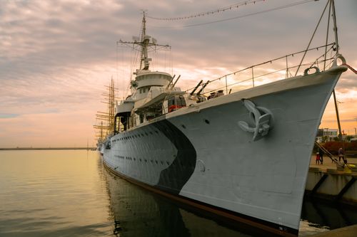 Free A large warship anchored at a peaceful harbor during sunset, reflecting on serene water. Stock Photo