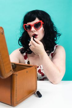 Stylish woman in heart-shaped sunglasses applying lipstick with a retro vibe.