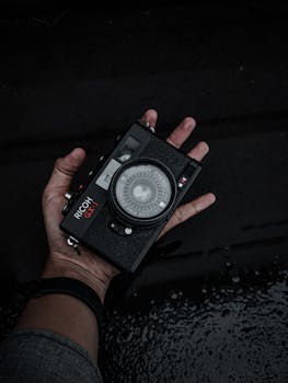 A close-up of a vintage camera in someone’s hand, showcasing retro design on a dark background.