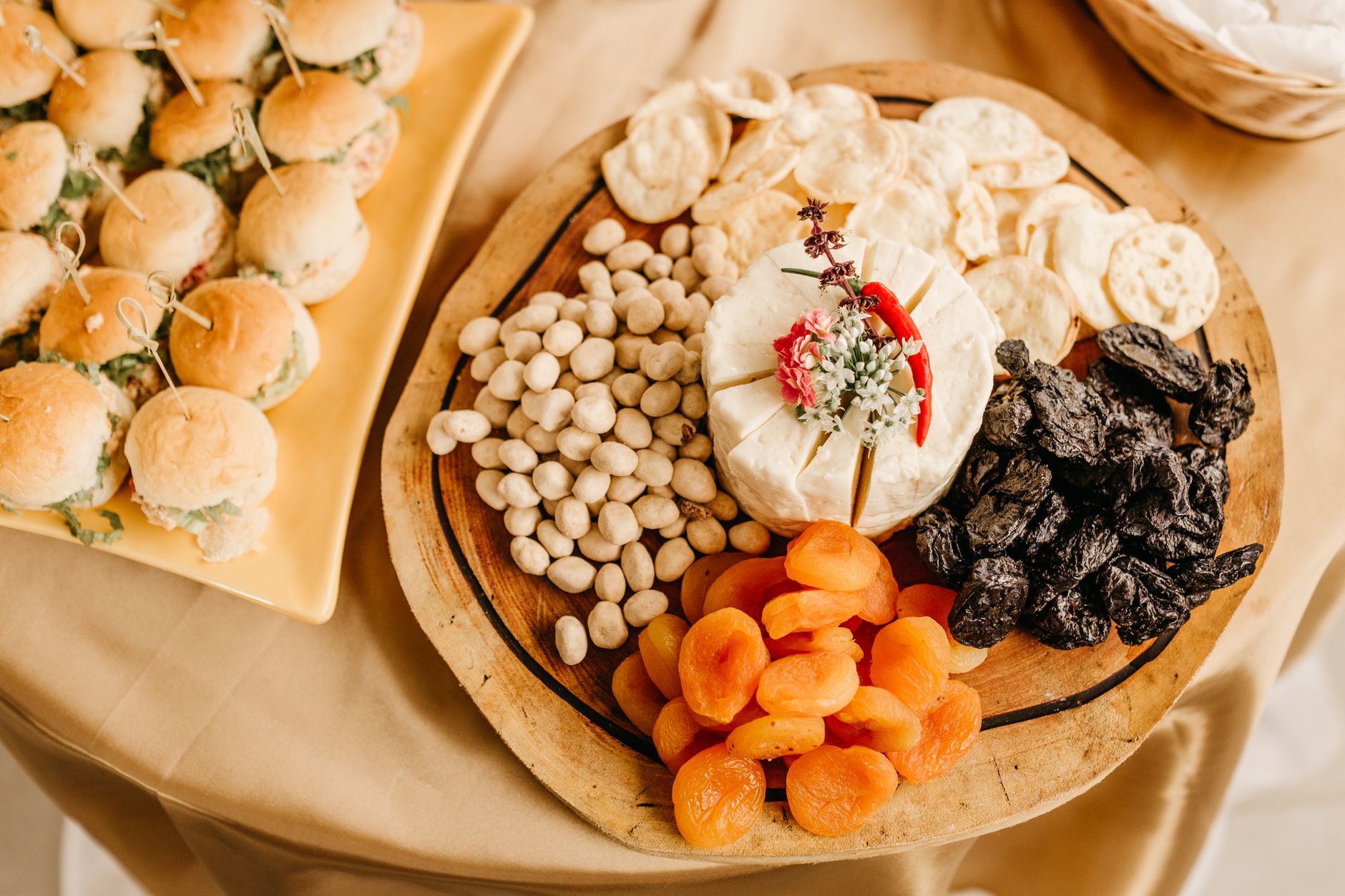Delectable cheese board featuring snacks and gourmet mini burgers on a beige tablecloth.